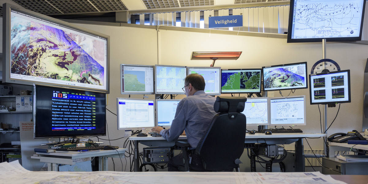KNMI-meteorologen kijken in de weerkamer naar weermodellen en data op beeldschermen