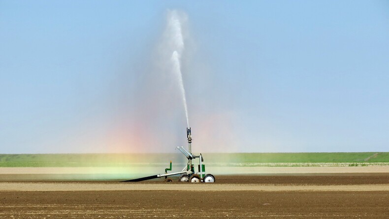 Op de foto is te zien hoe er water gesproeid wordt over droge landbouwgrond