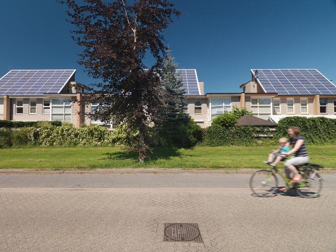 Zonnepanelen op daken van huizen in amersfoort en een vrouw met kind op fiets fietst over de straat