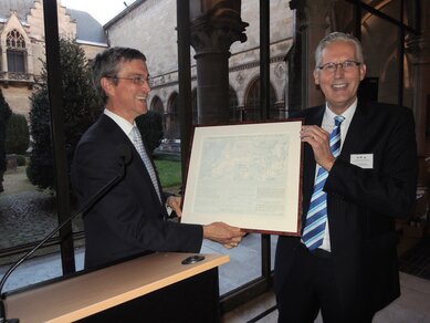 Algemeen directeur KMI Gellens (links) bewondert de replica van de originele KNMI-weerkaart van 31 juli 1913 die hij zojuist heeft ontvangen van hoofddirecteur Brouwer van het KNMI
