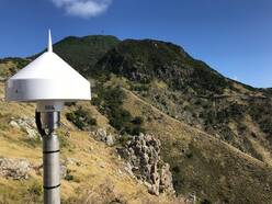 foto van een GNSS antenne op Saba, Caribisch Nederland, met de vulkaan Mount Scenery op de achtergrond