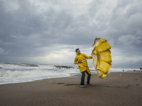 Man op strand met paraplu die door de wind omklapt