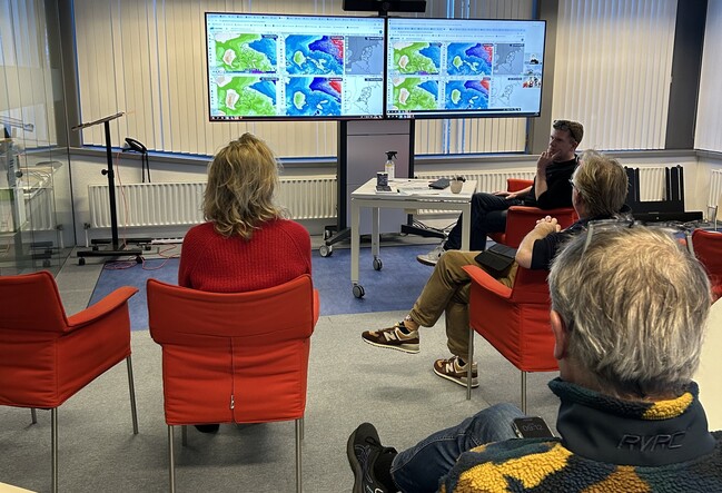 foto van mensen in vergadering voor een groot beeldscherm met weerkaarten.