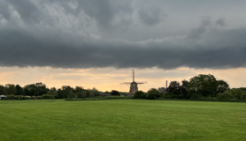 Nederlands landschap met een windmolen, groen gras en wolken 