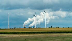 Windturbines met op de achtergrond electriciteitscentrale met rokende schoorstenen