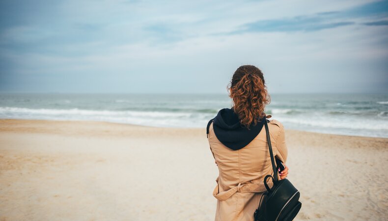 Vrouw met jas aan op het strand