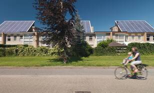 Zonnepanelen op daken van huizen in amersfoort en een vrouw met kind op fiets fietst over de straat