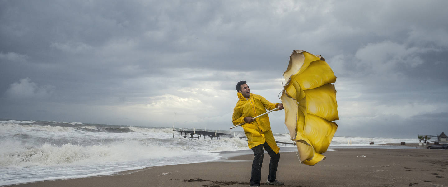 man trotseert storm aan de kust met dubbelgeklapte paraplu