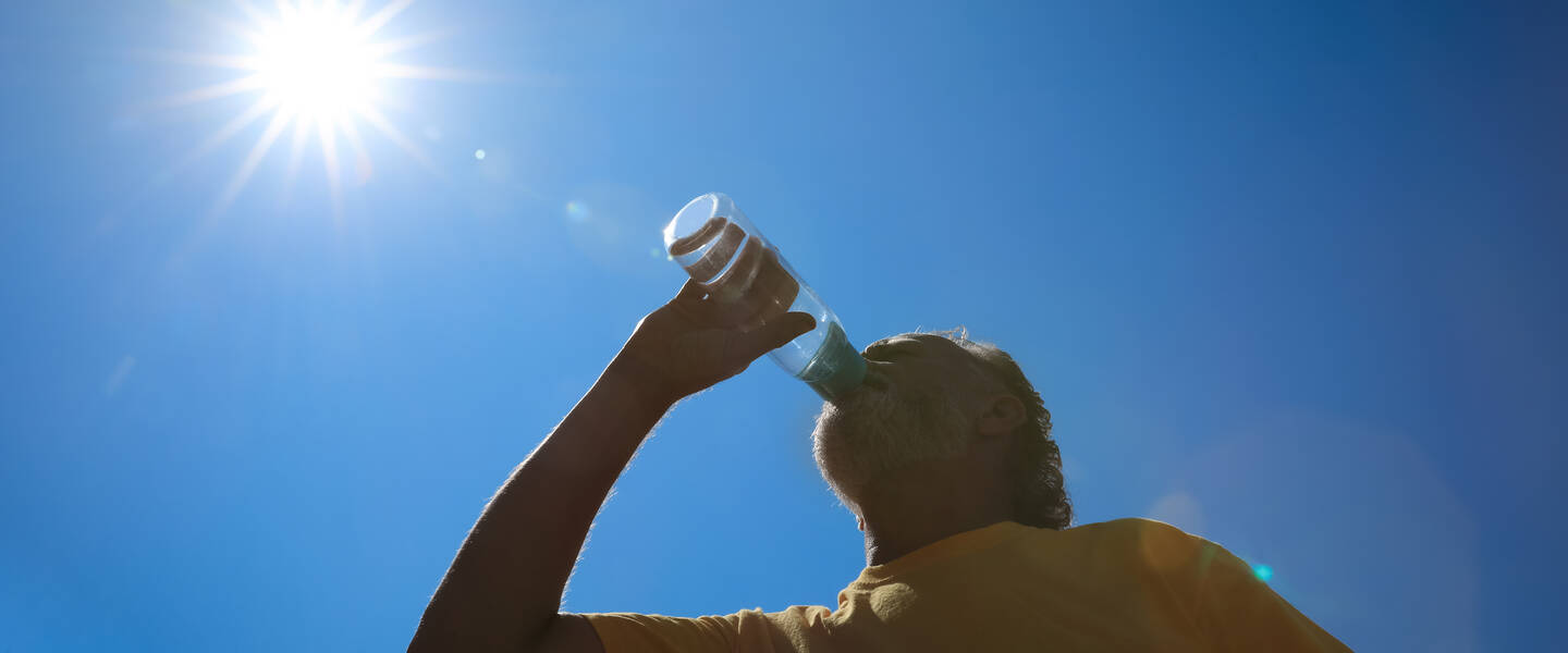Man drinkt water uit een fles onder een strakblauwe, zonnige hemel