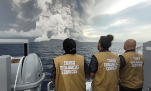 Mensen kijken vanaf een schip naar utbarsting van de Hunga Tonga Vulkaan