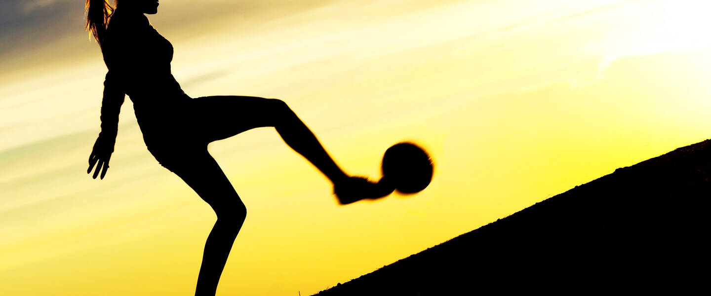 Silhouette van een vrouw die een bal tegen een heuvel op schiet