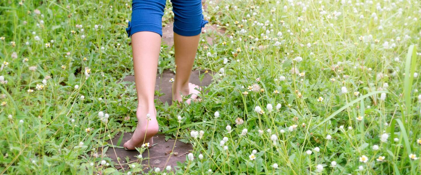 Iemand loopt op blote voeten door het gras, je ziet alleen de benen van achteren