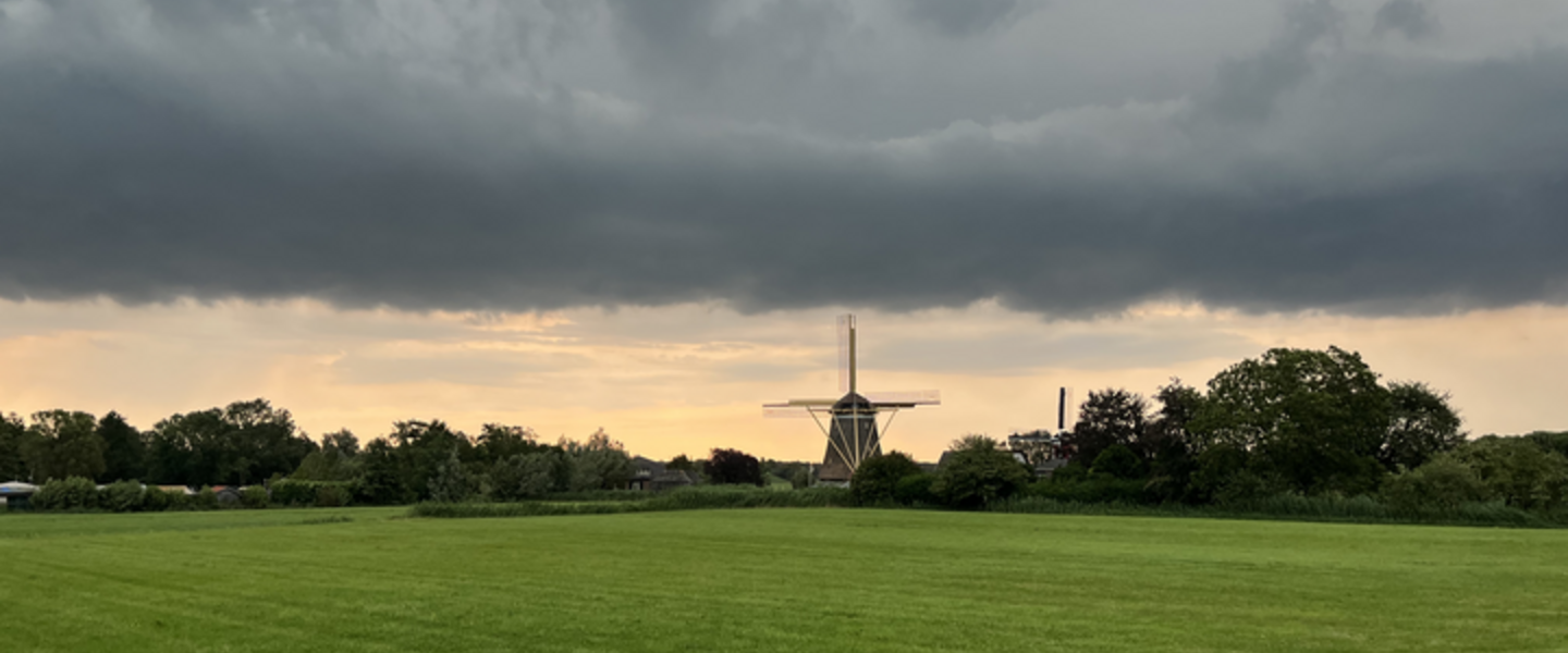 Nederlands landschap met een molen, groen gras en een wolk 