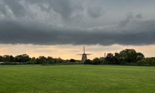 Nederlands landschap met een molen, groen gras en een wolk 