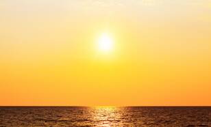 Zon boven oceaan in feloranje gekleurde lucht