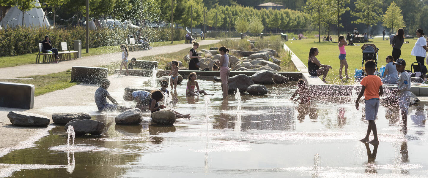 Mensen en kinderen zoeken verkoeling bij het water in Tilburg. 