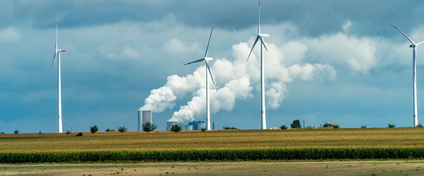 Windturbines met op de achtergrond electriciteitscentrale met rokende schoorstenen