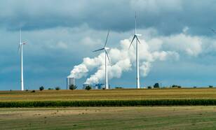 Windturbines met op de achtergrond electriciteitscentrale met rokende schoorstenen
