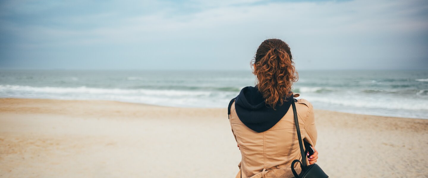 Vrouw met jas aan op het strand