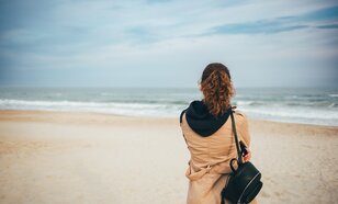 Vrouw met jas aan op het strand