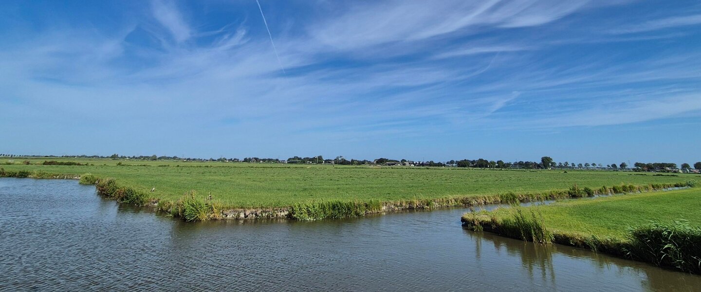 Foto van zonnig weiland, water zon en wolken in petten.